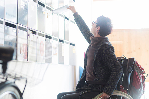 woman-in-wheelchair-at-post-office-mailing-letter-living-with-a-neurological-condition_495x328