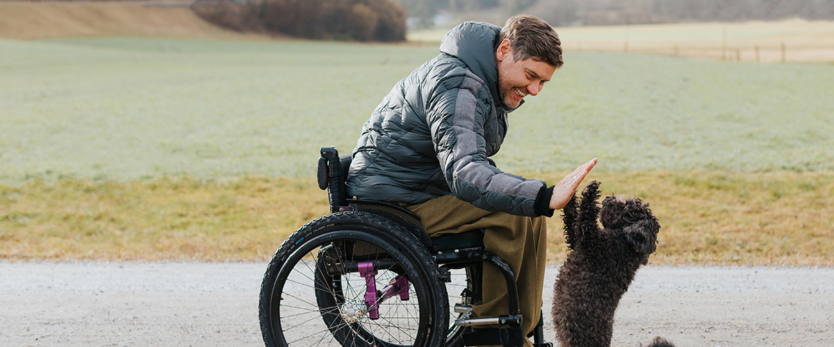 Man-in-wheel-chair-high-fiving-poodle-spinal-injuries-awareness-month
