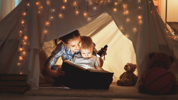 mother-and-young-child-under-tent-reading-Hollister-ostomy-pediatric-care-tips-575x325