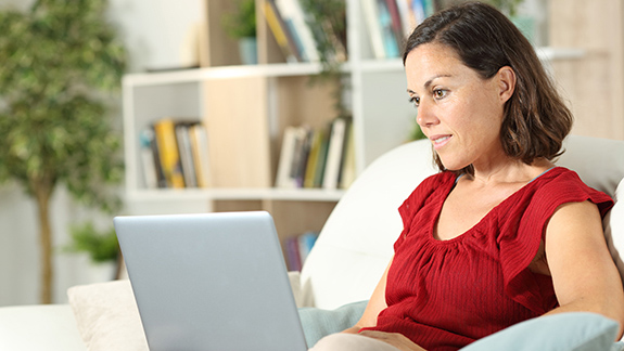 woman-relaxed-on-couch-watching-laptop-Hollister-ostomy-educational-theatre-videos-575x325